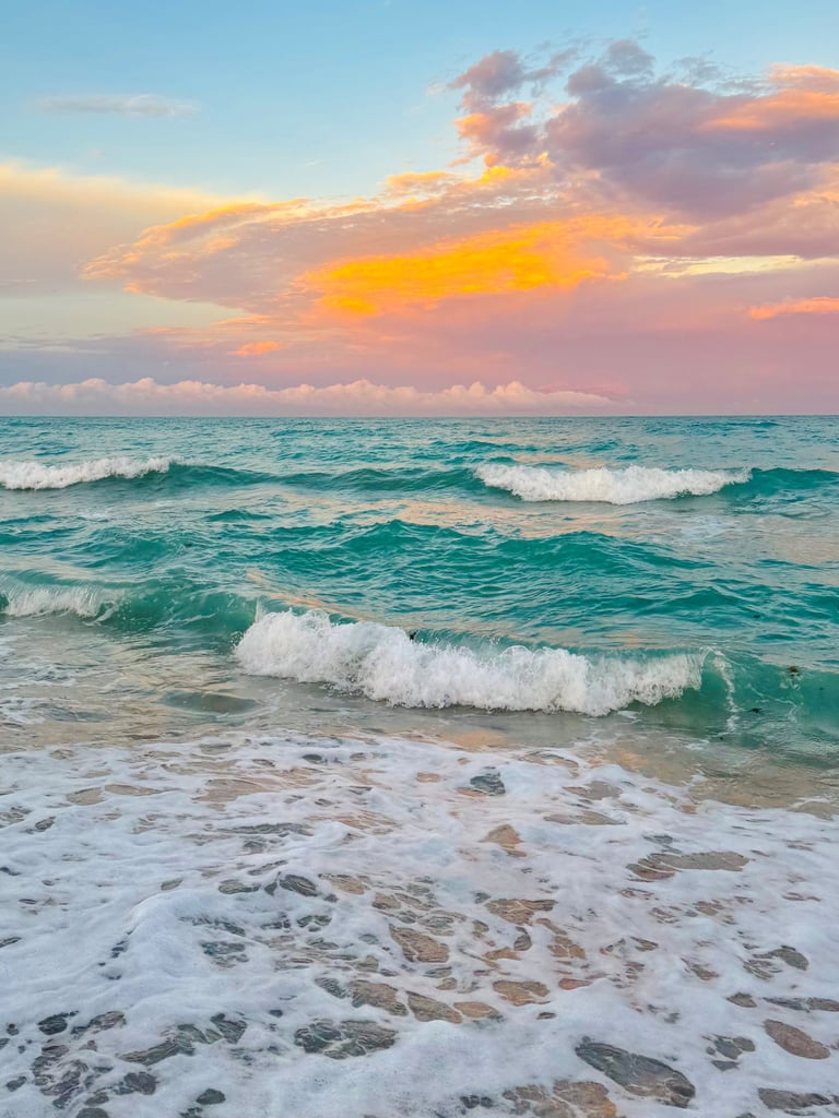 Amazing colorful sky like cotton candy colors; clouds and sky meet at the horizon with gentle waves at the shoreline.