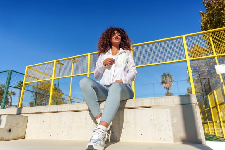 Young woman with curly hair wearing sportswear, sitting on concrete steps in an urban environment
